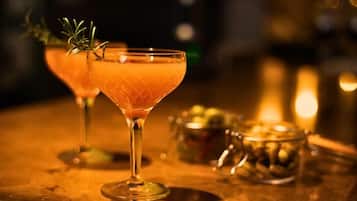 A bar setting with two cocktail glasses, one with a garnish, and a metal container with olives on a wooden surface.