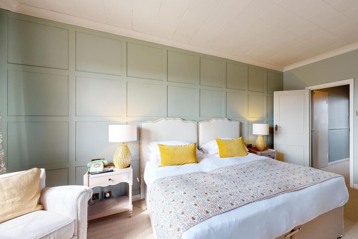 A hotel room with a large bed, two bedside tables with lamps, a chair, a wardrobe, and a mirror.