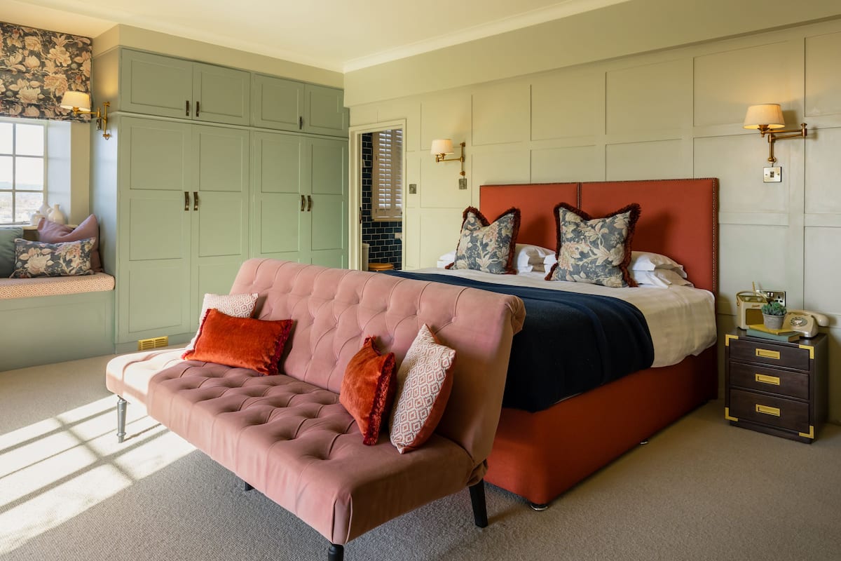 A bedroom with a large bed, a pink sofa, and a green wardrobe.
