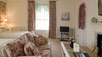 A hotel room with a sofa, a television, a fireplace, and a bookshelf.