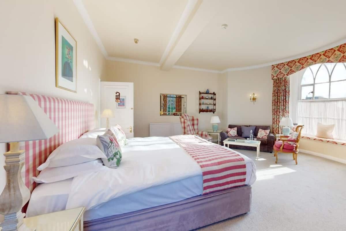 A hotel room with a bed, a desk with a television, a chair, a sofa, and a window with curtains.