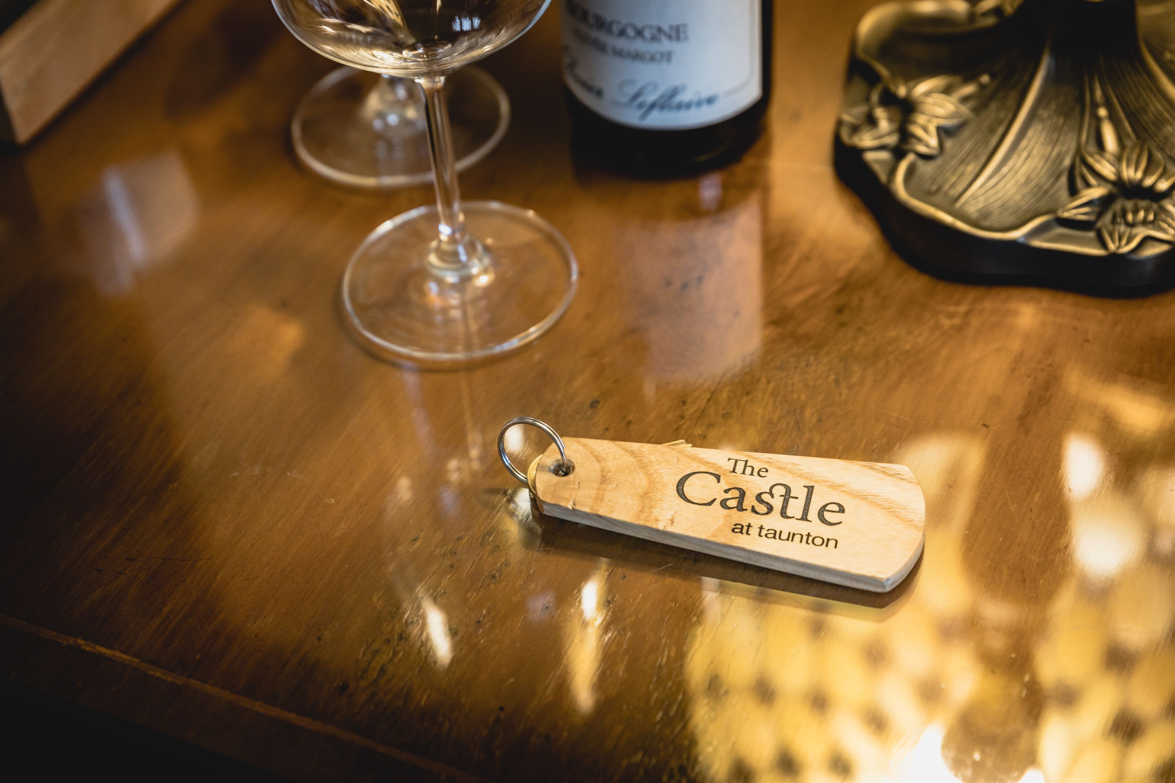 A wooden bar counter with a wine glass, a bottle of wine, and a wooden keychain with text.