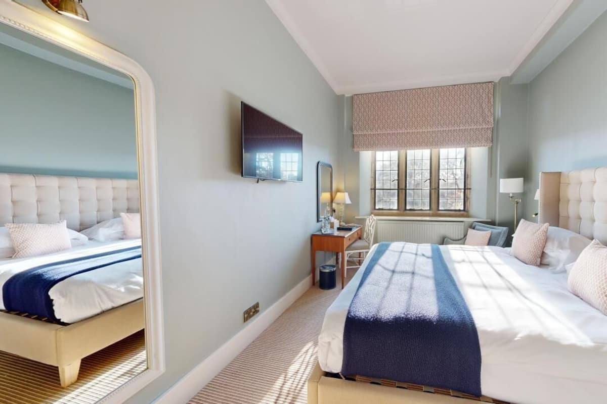 A hotel room with two beds, a large mirror, a television, and a window with a view.