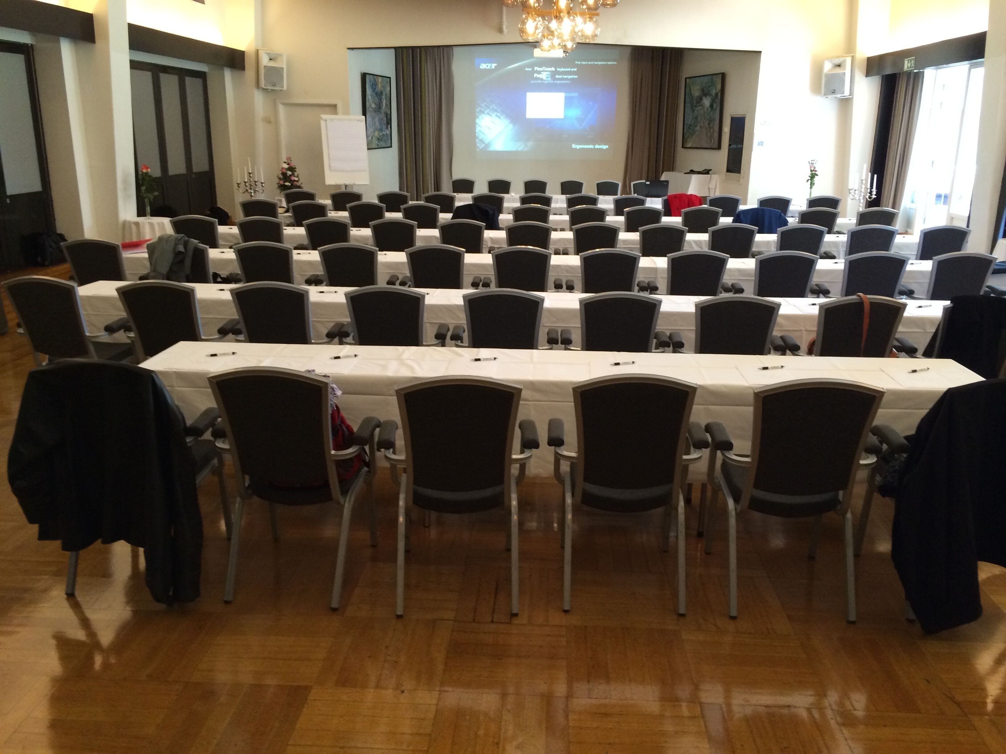 A conference room with rows of chairs and tables, a projector screen, and a whiteboard.