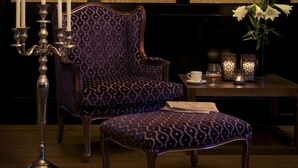 A room with a patterned armchair, a matching ottoman, a candelabra with lit candles, and wall-mounted sconces. - Vinger Hotell (Kongsvinger)