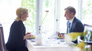 A dining table set for two with a vase of flowers, clear glassware, and a candle. - Vinger Hotell (Kongsvinger)