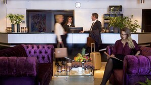 A lobby with plush purple sofas, a reception desk, and a fruit basket on a table. - Vinger Hotell (Kongsvinger)