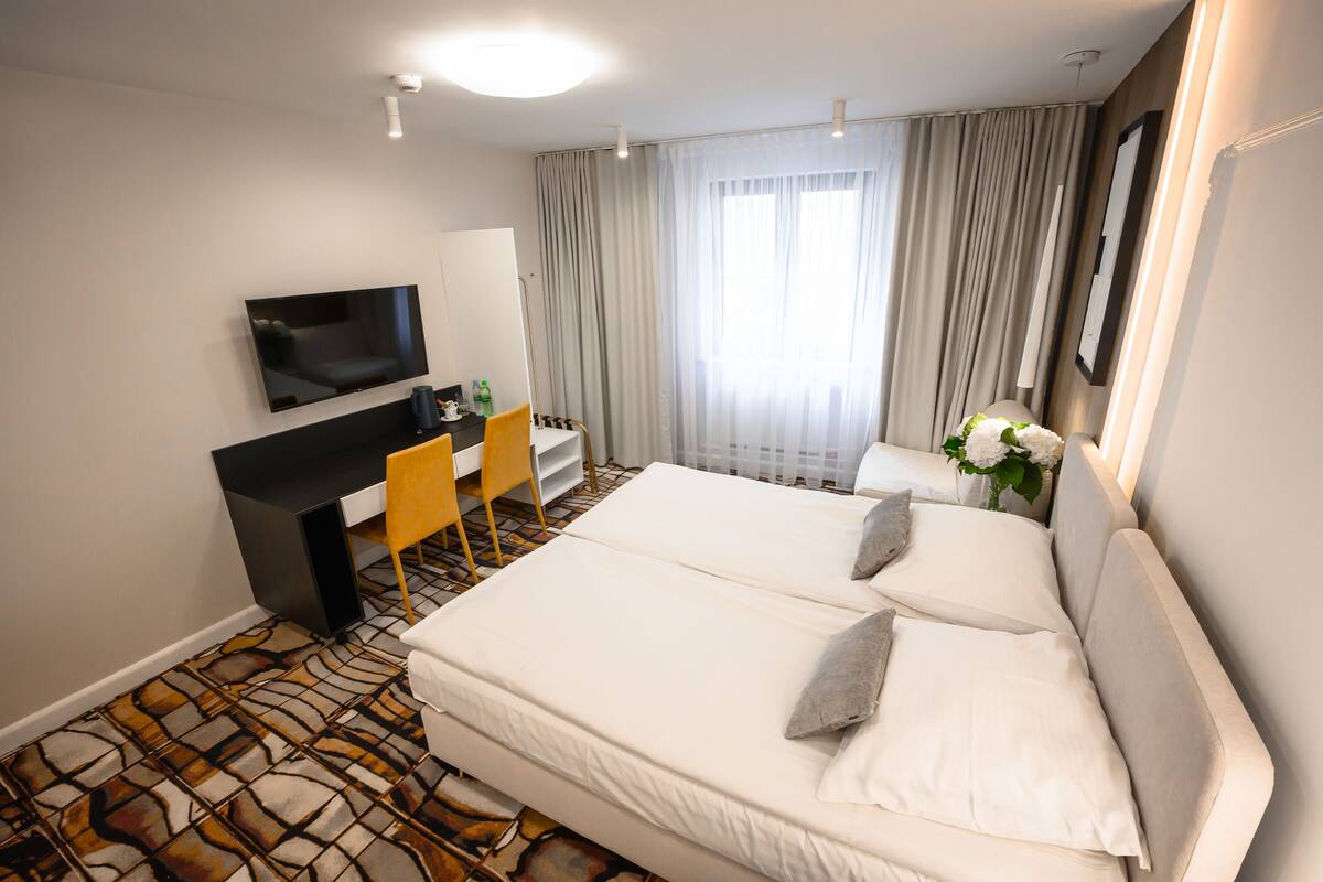 A hotel room with a bed, a desk, a chair, a TV, and a window with curtains.