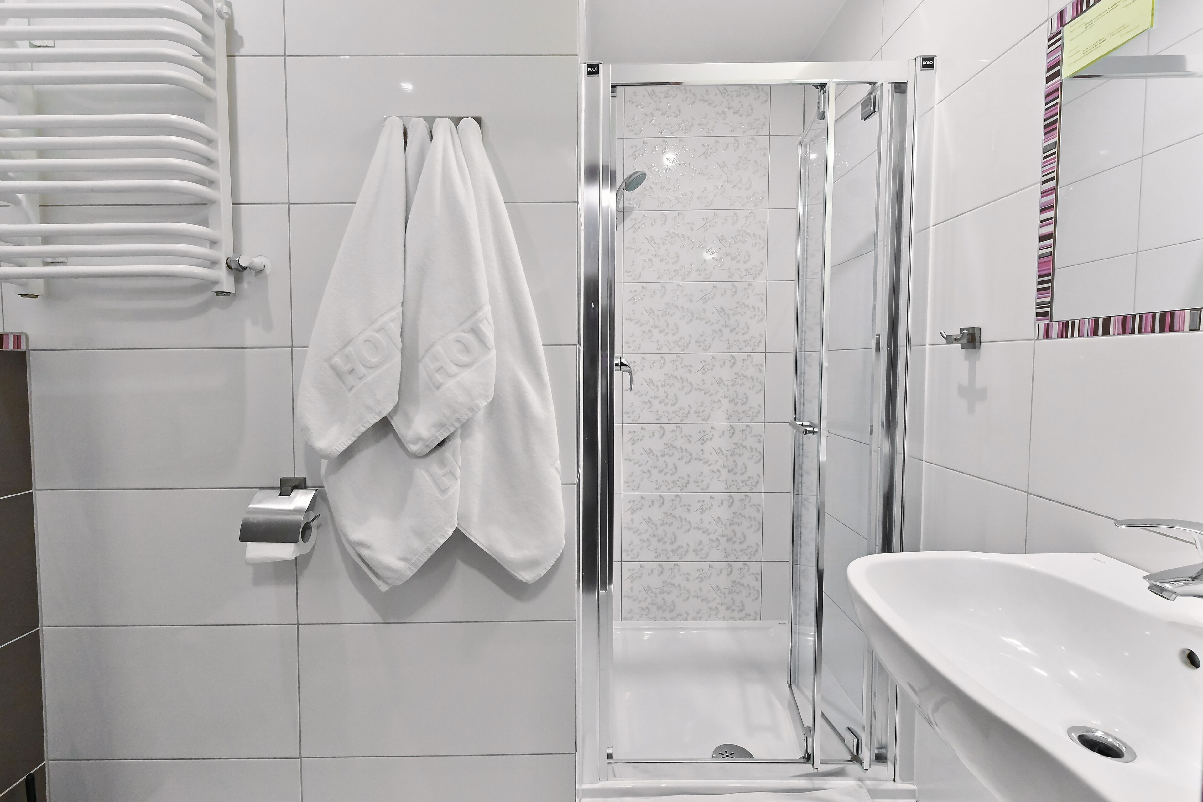 A modern bathroom with a glass shower enclosure, a white sink, and a towel rack with two towels.