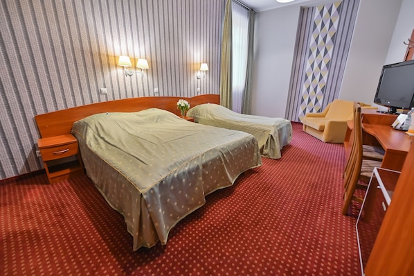Quarto de hotel com duas camas, uma escrivaninha com computador e televisão.