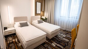 Una habitación de hotel con dos camas individuales, una mesita de noche, un escritorio y una silla.