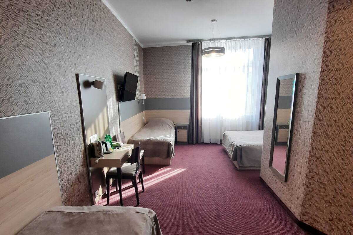 A hotel room with two beds, a desk with a chair, a television, and a large mirror.