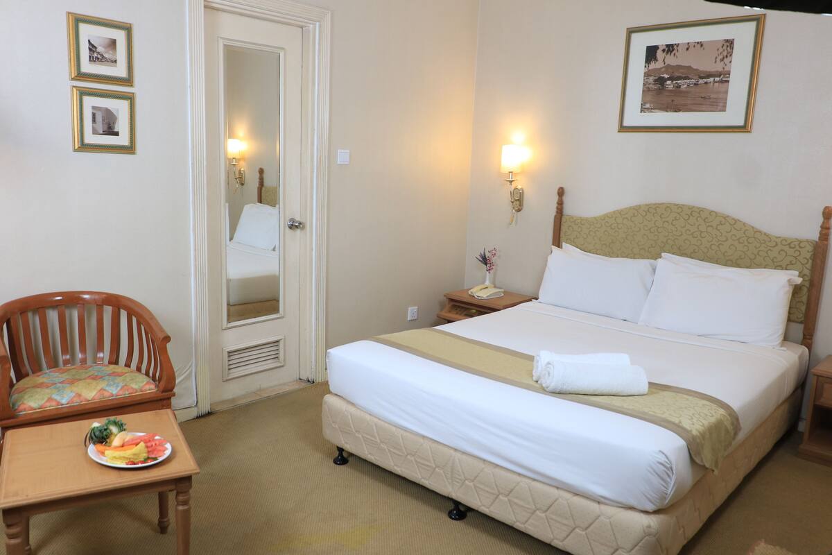 A hotel room with a bed, a chair, a small table with a plate of food, and a mirror.
