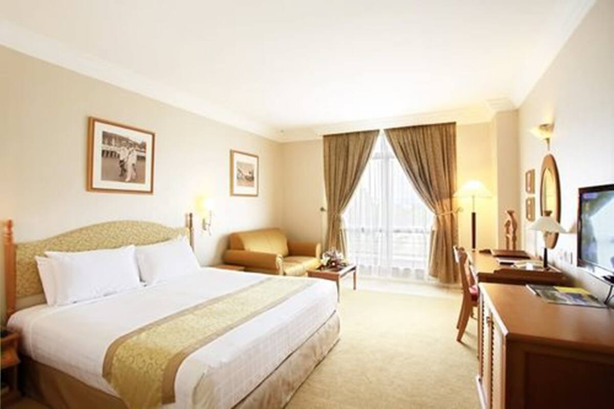 A hotel room with a large bed, a sofa, a desk with a computer, and a television.