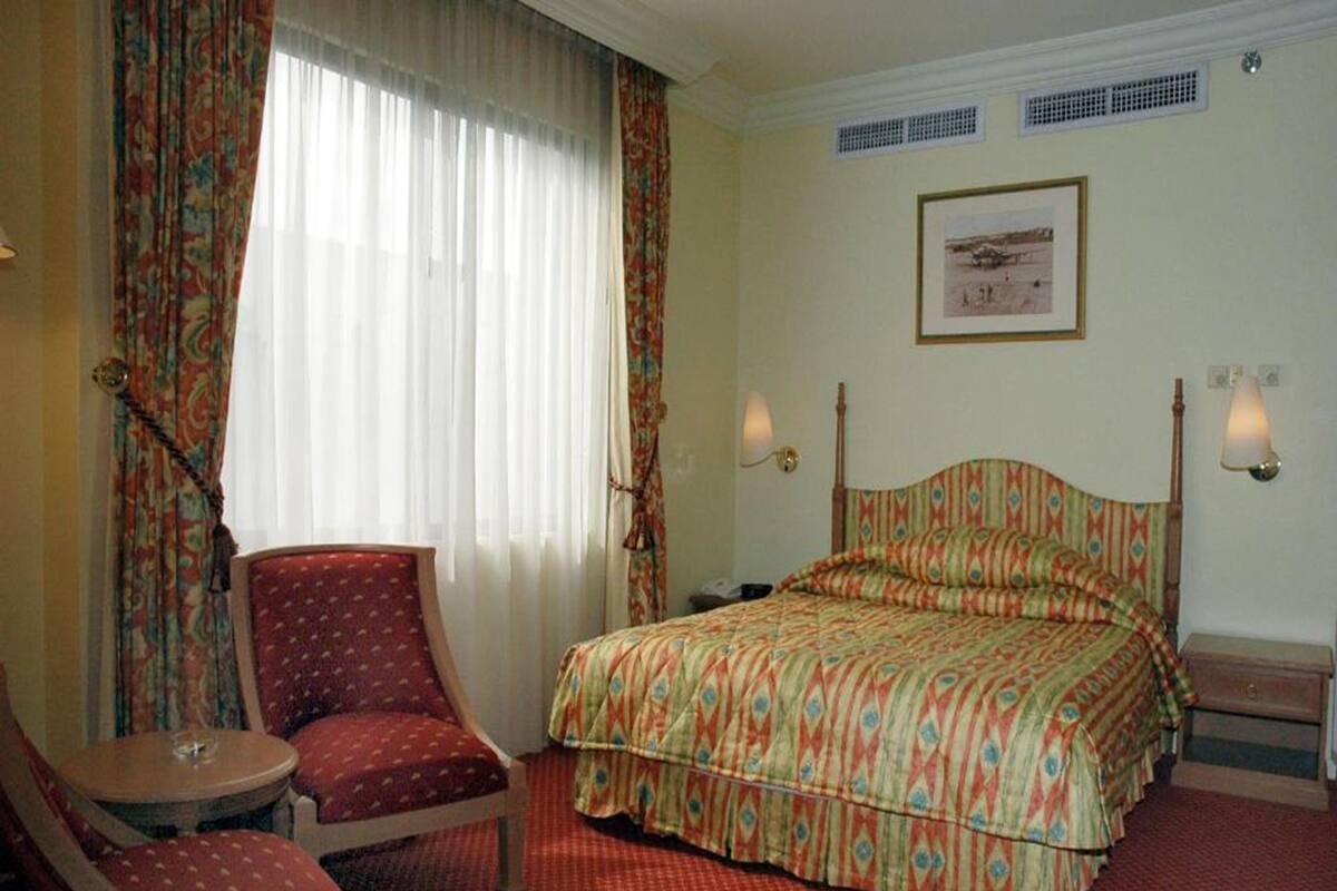 A hotel room with a bed, a chair, a small table, and a window with curtains.