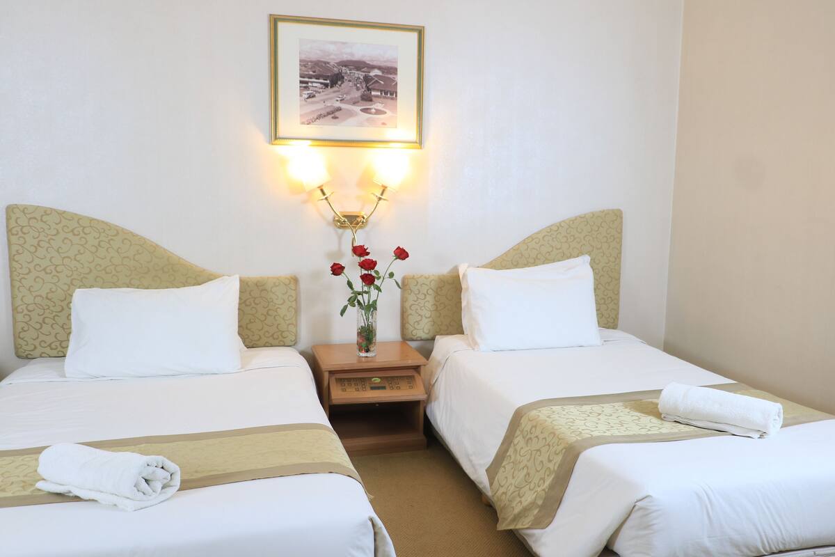 A hotel room with two beds, a nightstand with a vase of red roses, and a framed picture on the wall.