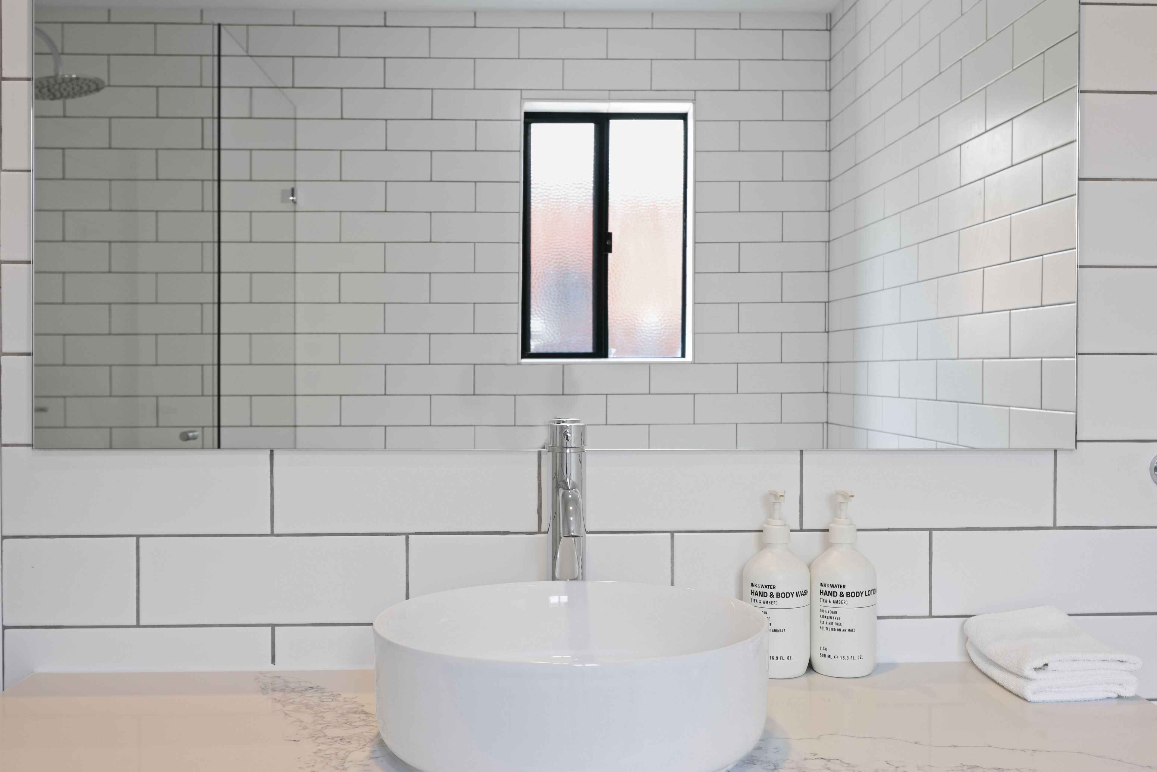 A modern bathroom with a large white sink, a glass shower enclosure, and a window with frosted glass.