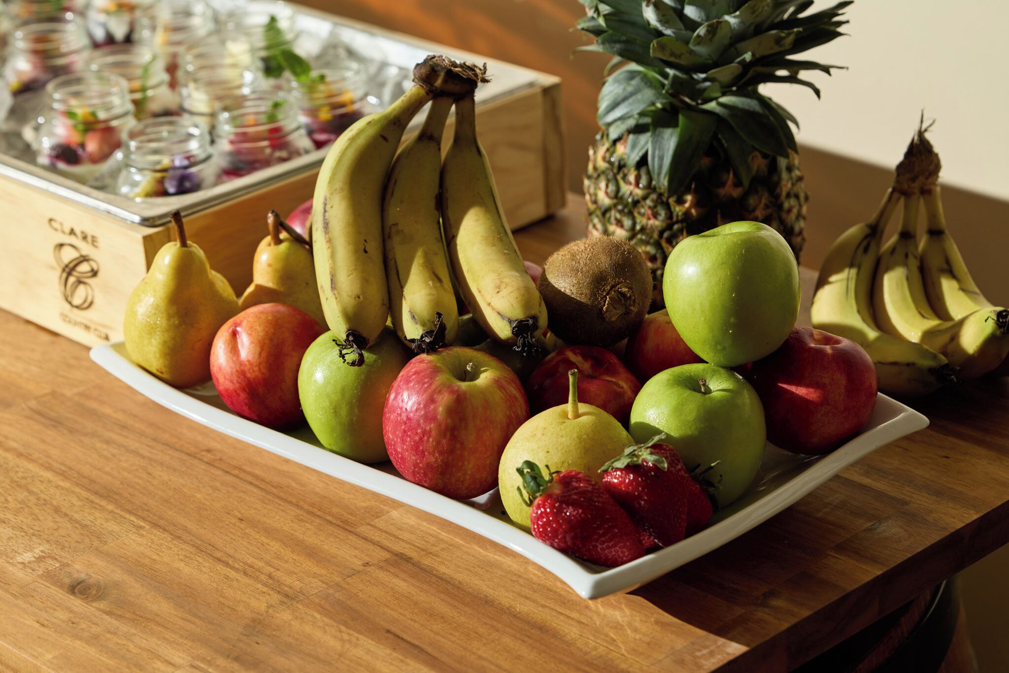 A wooden table with a variety of fruits including bananas, apples, and a pineapple.