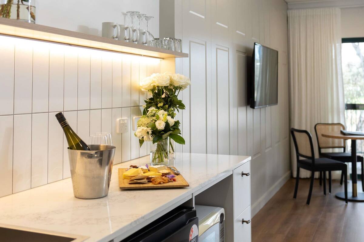 A modern kitchen with a marble countertop, a wine bottle in a bucket, a vase of flowers, and a TV mounted on the wall.