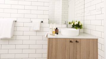 Une salle de bain avec des carreaux de céramique blancs rectangulaires, un lavabo blanc, un meuble en bois et un miroir.