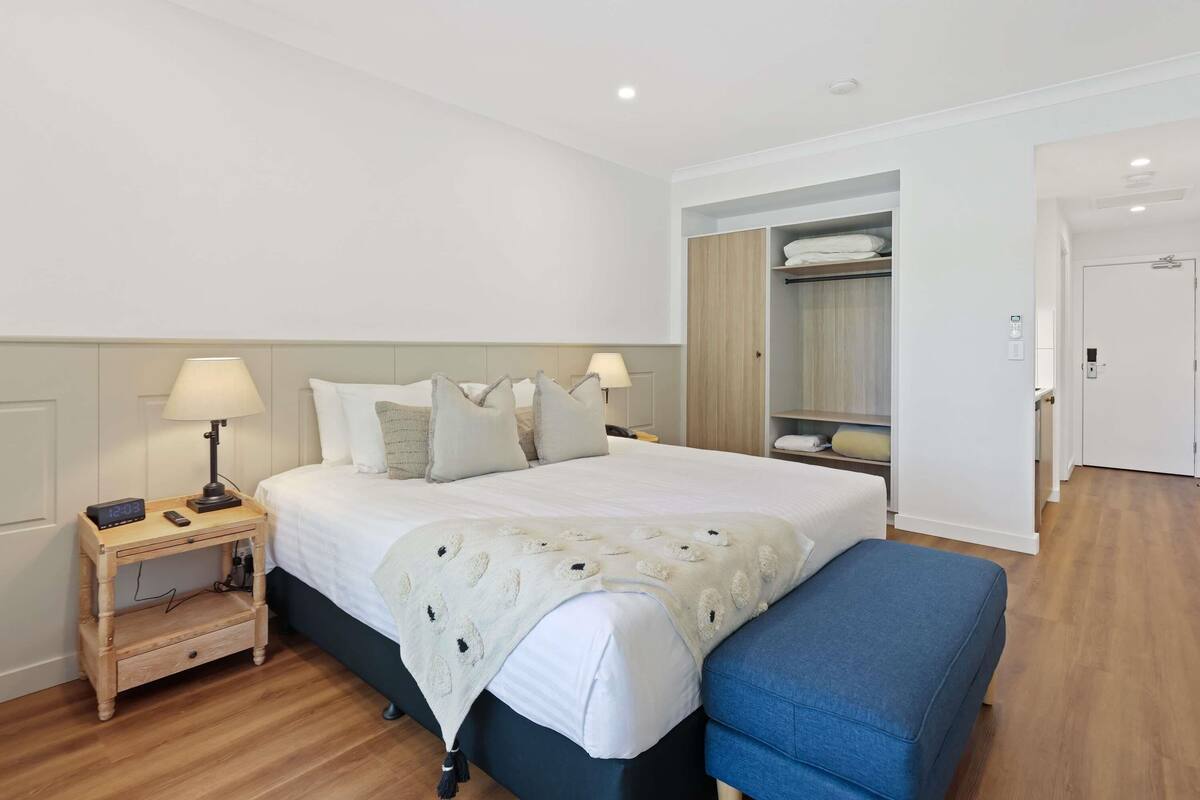 A hotel room with a bed, bedside tables, a bench, a wardrobe, and a door.