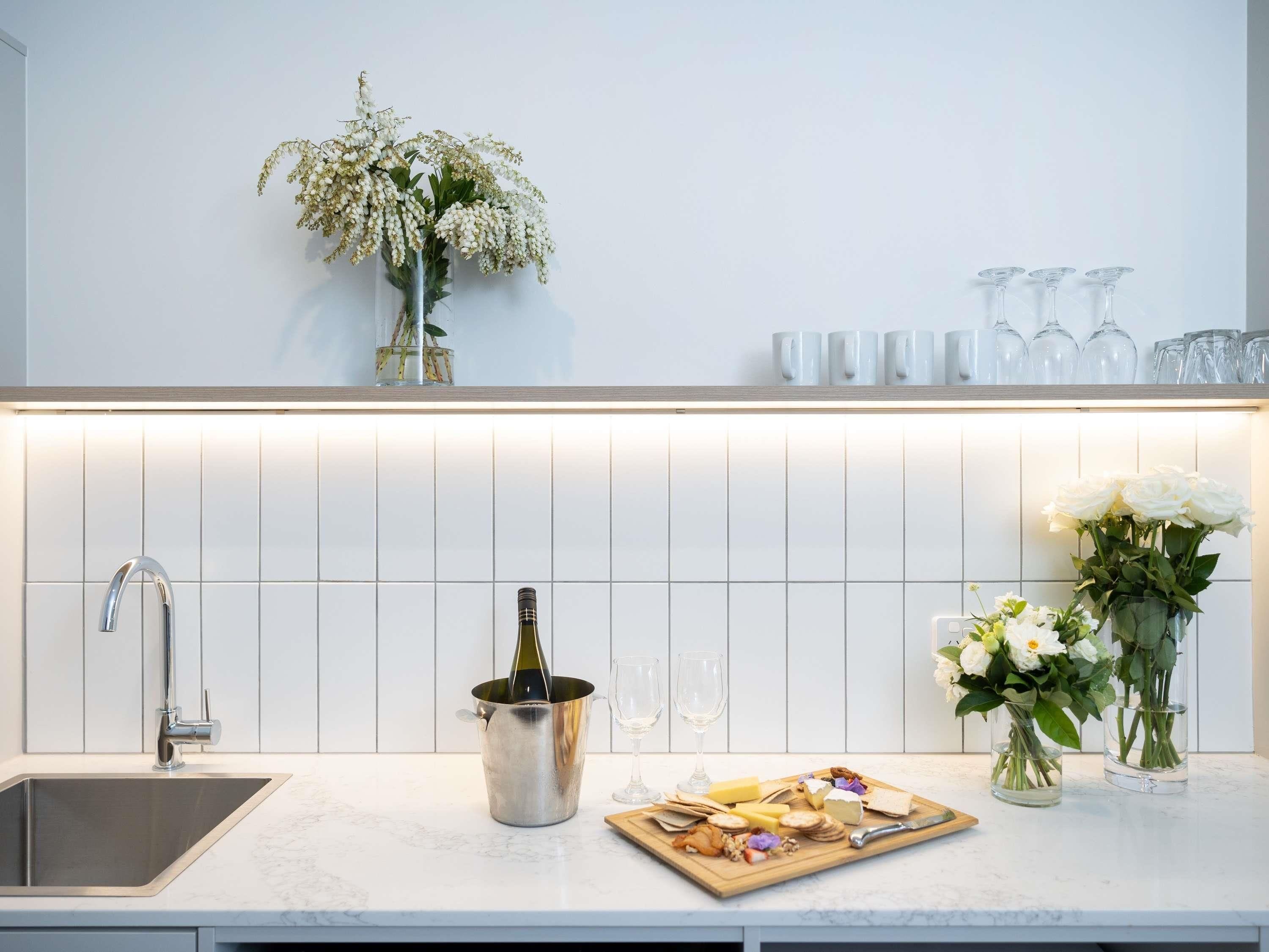 Una cocina moderna con un lavamanos integrado, una botella de vino en un cubo, una tabla de quesos y flores decorativas.