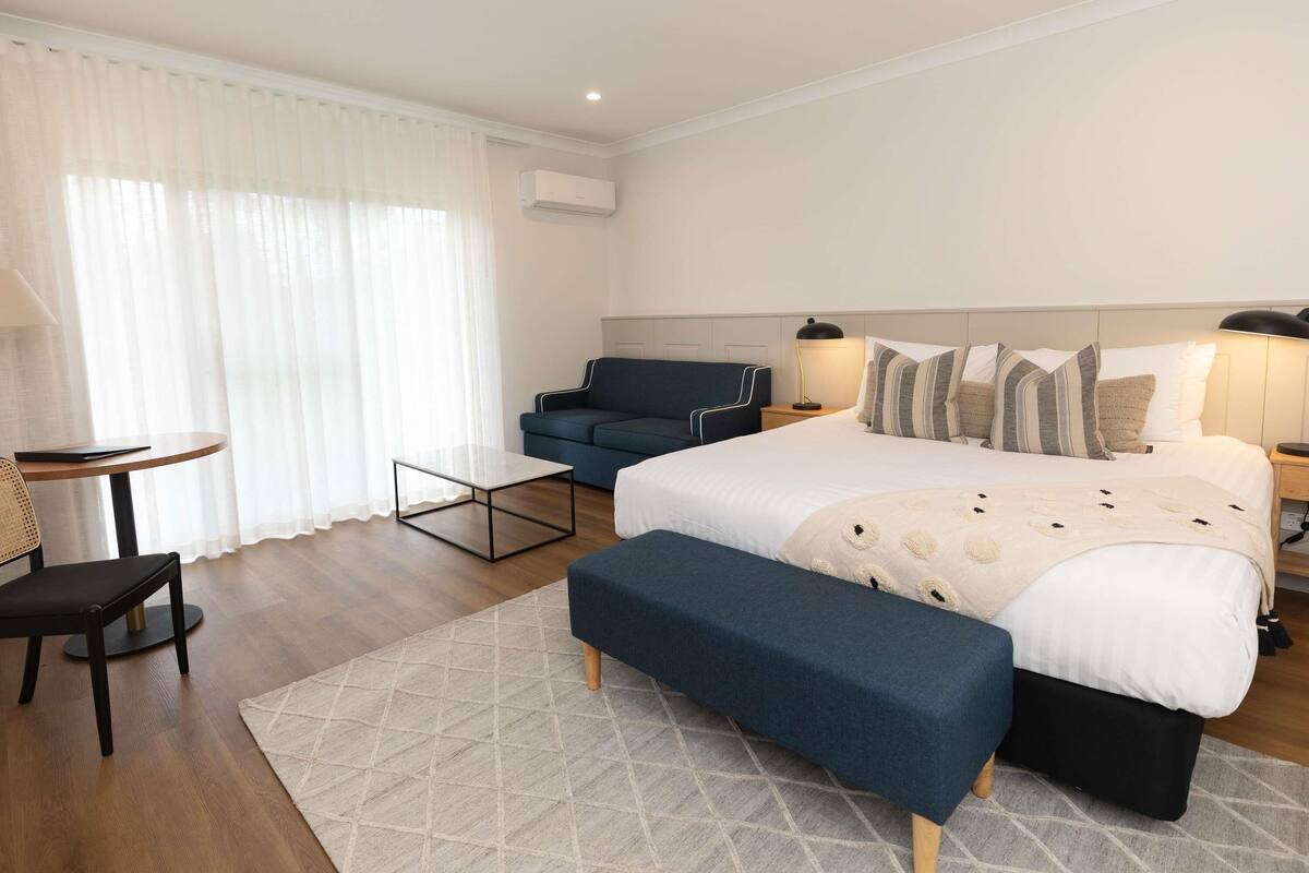 A modern hotel room with a bed, a desk, a chair, and a sofa.