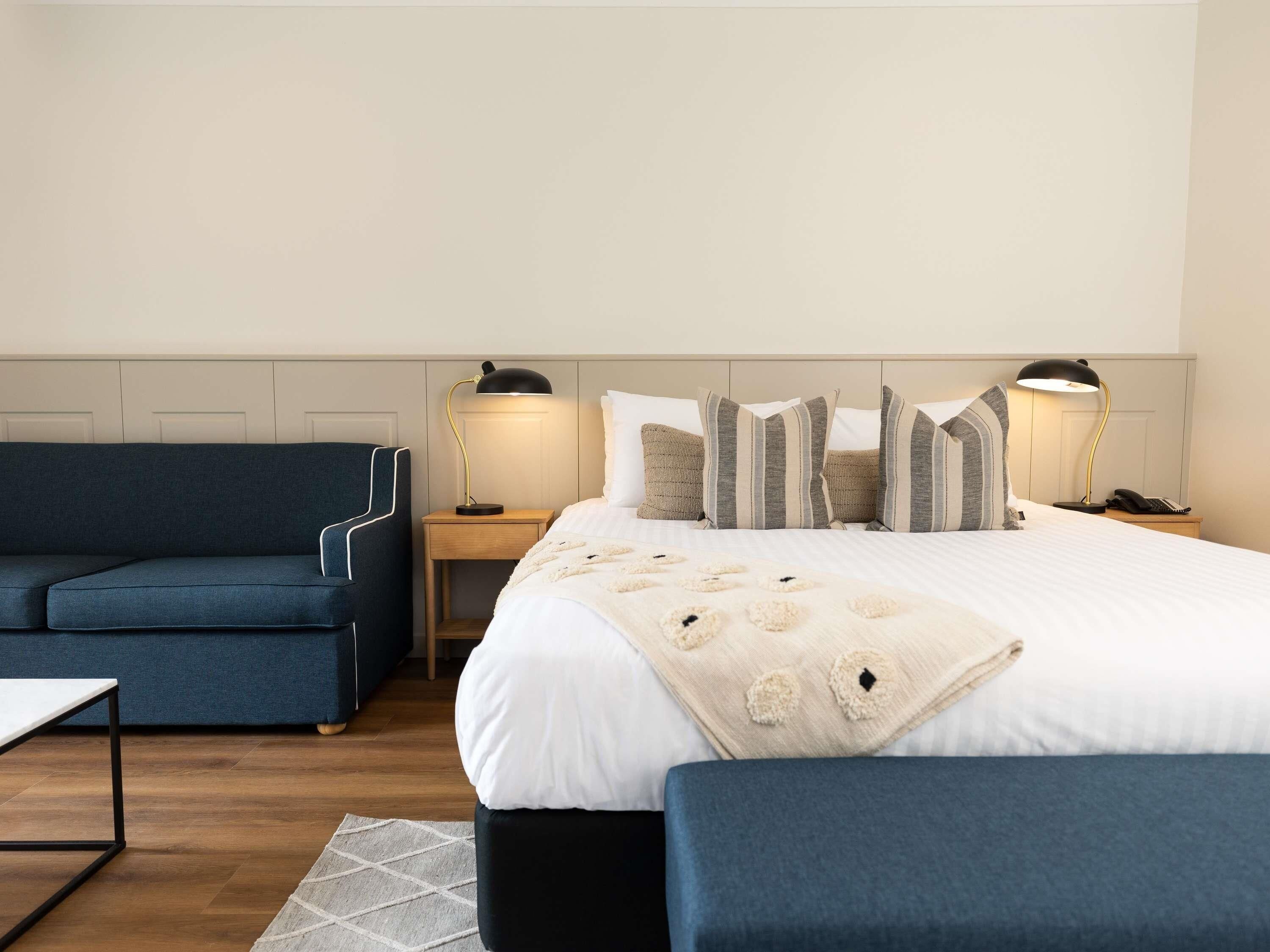 A hotel room with a bed, a blue sofa, a small table, and two bedside lamps.