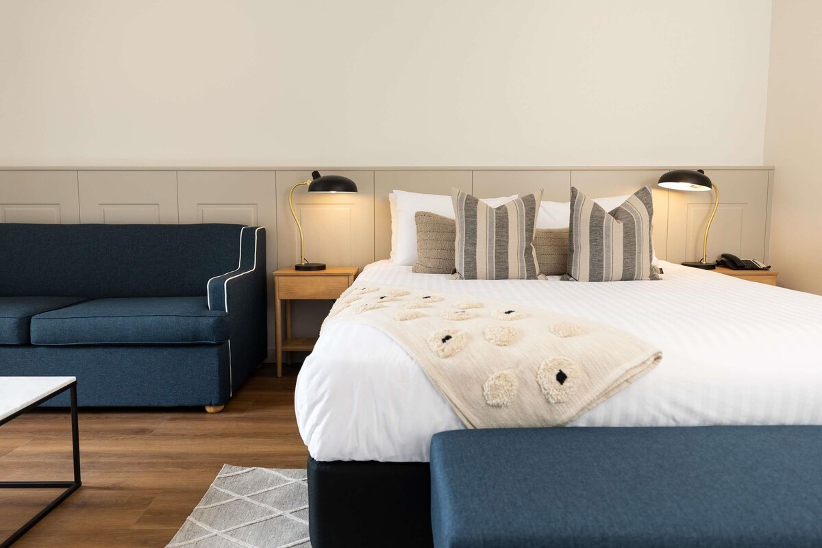 A hotel room with a bed, a blue sofa, a small table, and two bedside lamps.