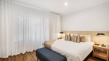 A neatly arranged bedroom with a large bed, a bedside table with a lamp, and a bench.