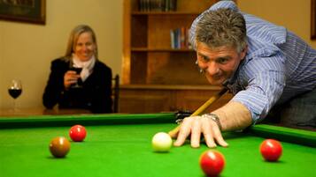 A person playing pool in a room with a green pool table, surrounded by bookshelves and a framed picture on the wall.