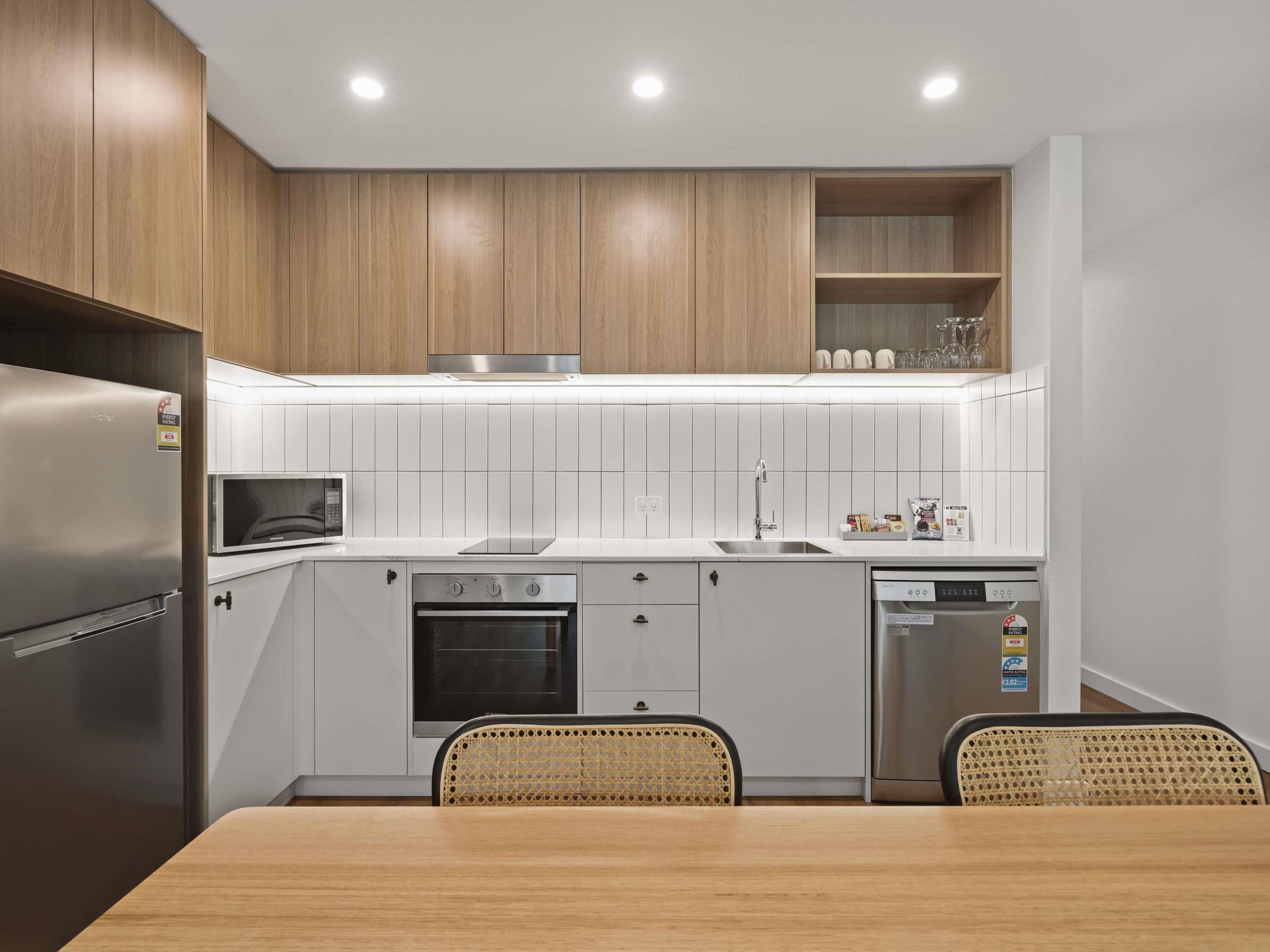 A modern kitchen with wooden cabinets, a stainless steel refrigerator, a microwave, an oven, a sink, and a dishwasher.