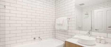 A modern bathroom with white subway tiles, a freestanding bathtub, a vanity with a round sink, and a large mirror.