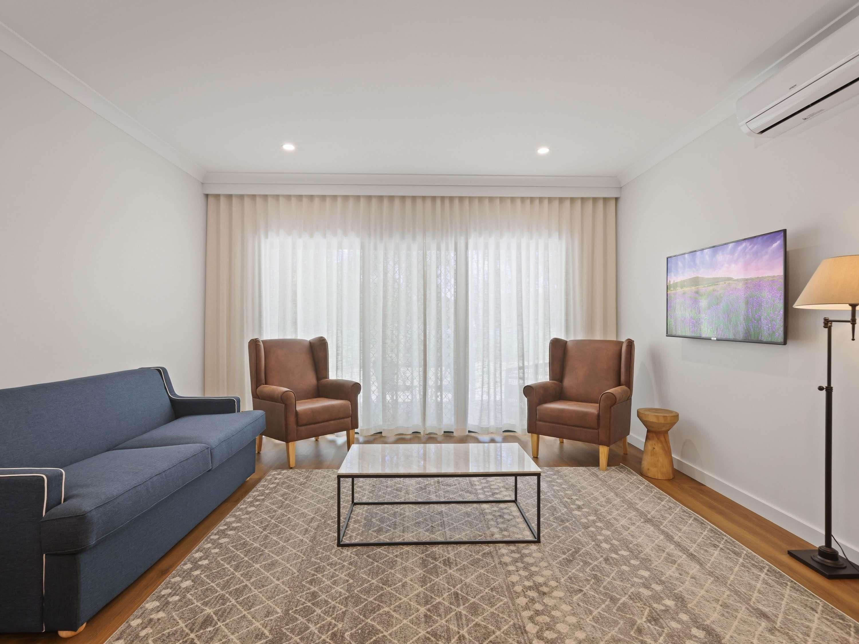 Una sala de estar moderna con un sofá azul, dos sillones de cuero, una mesa de centro y una lámpara de pie.