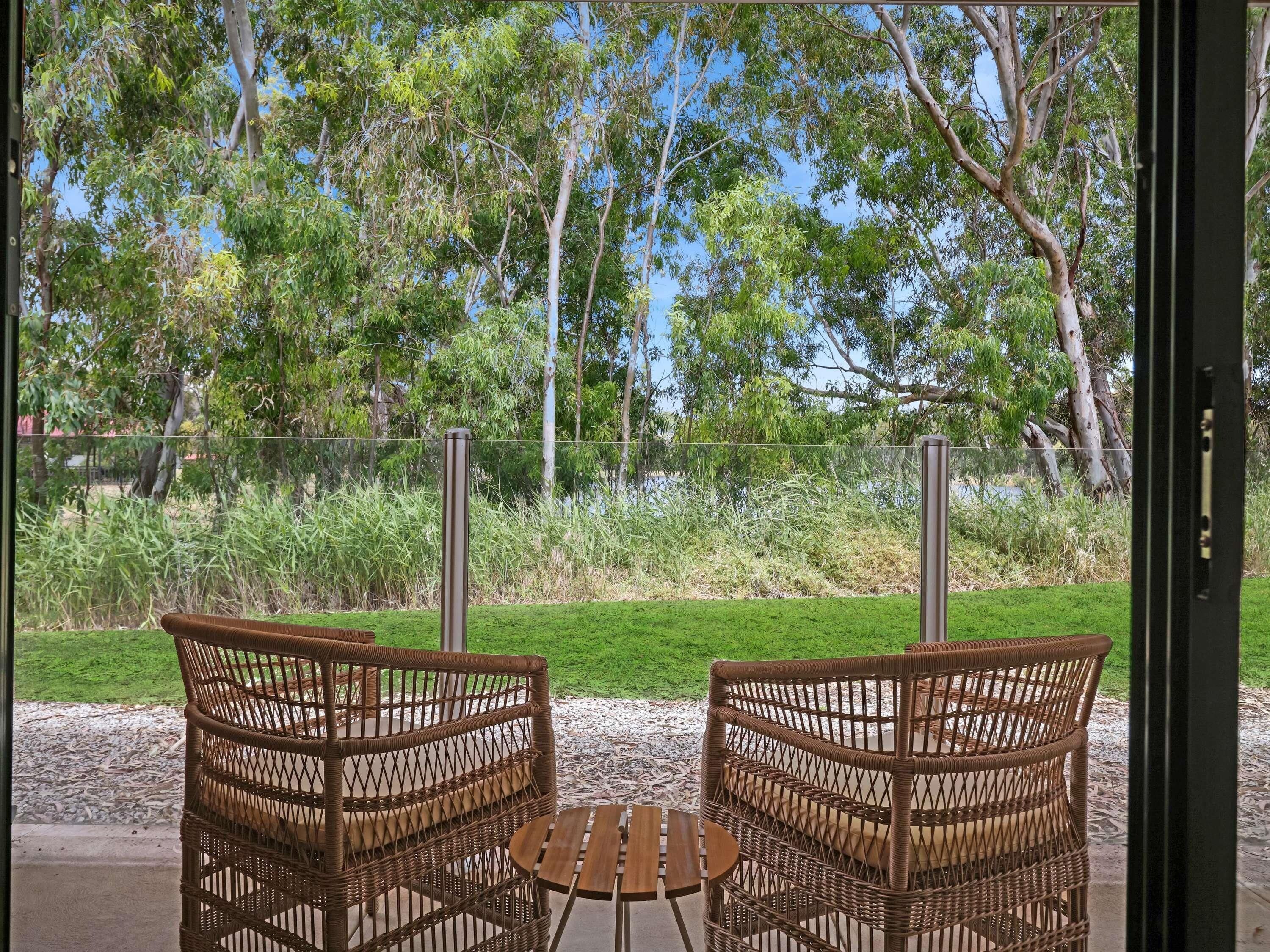 An outdoor seating area with wicker chairs and a small round table, surrounded by a grassy lawn and trees.
