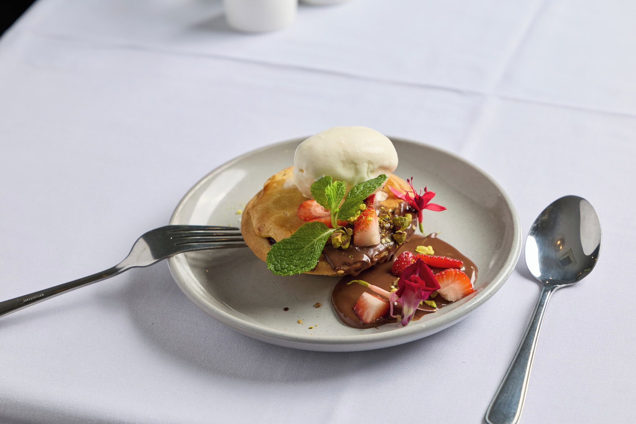 A dessert plate with a scoop of ice cream, strawberries, mint, and chocolate sauce.