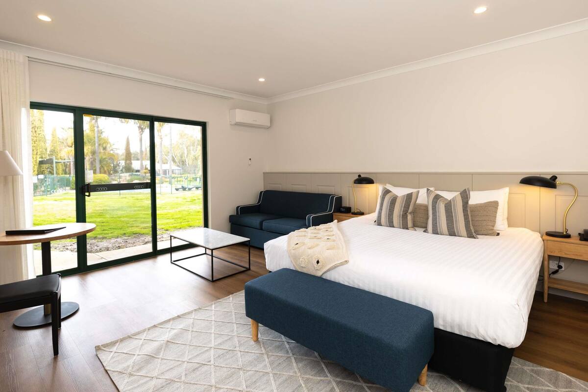 A modern hotel room with a large bed, a sofa, a small table, and a bench.