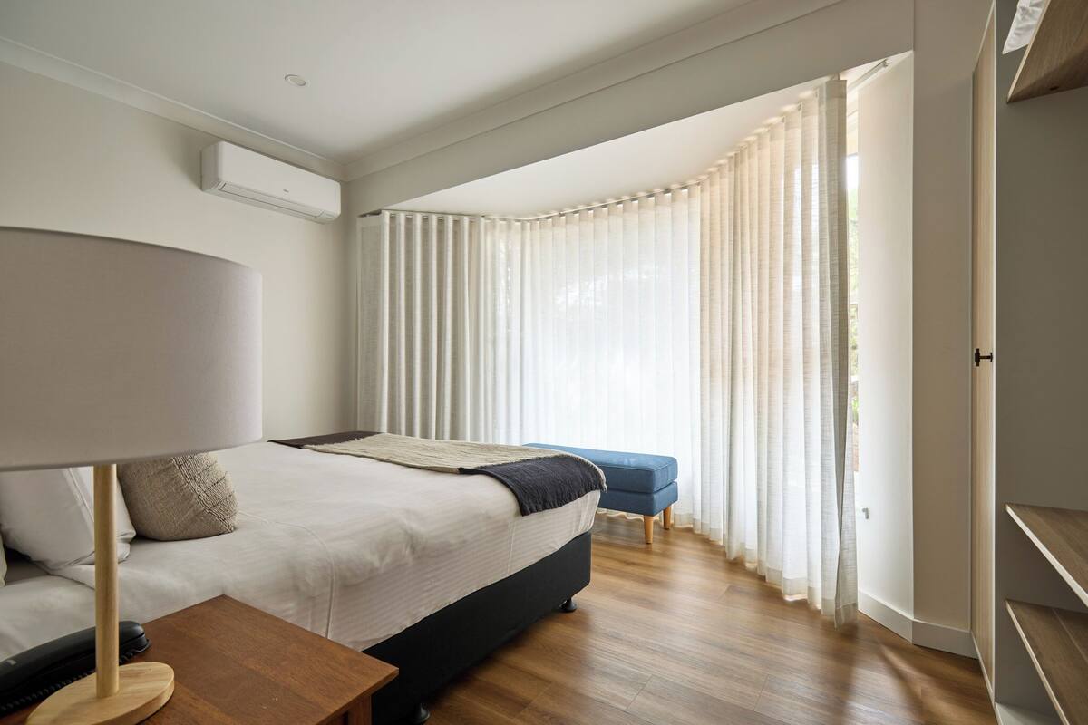 A bedroom with a bed, bedside table, lamp, and a window with curtains.