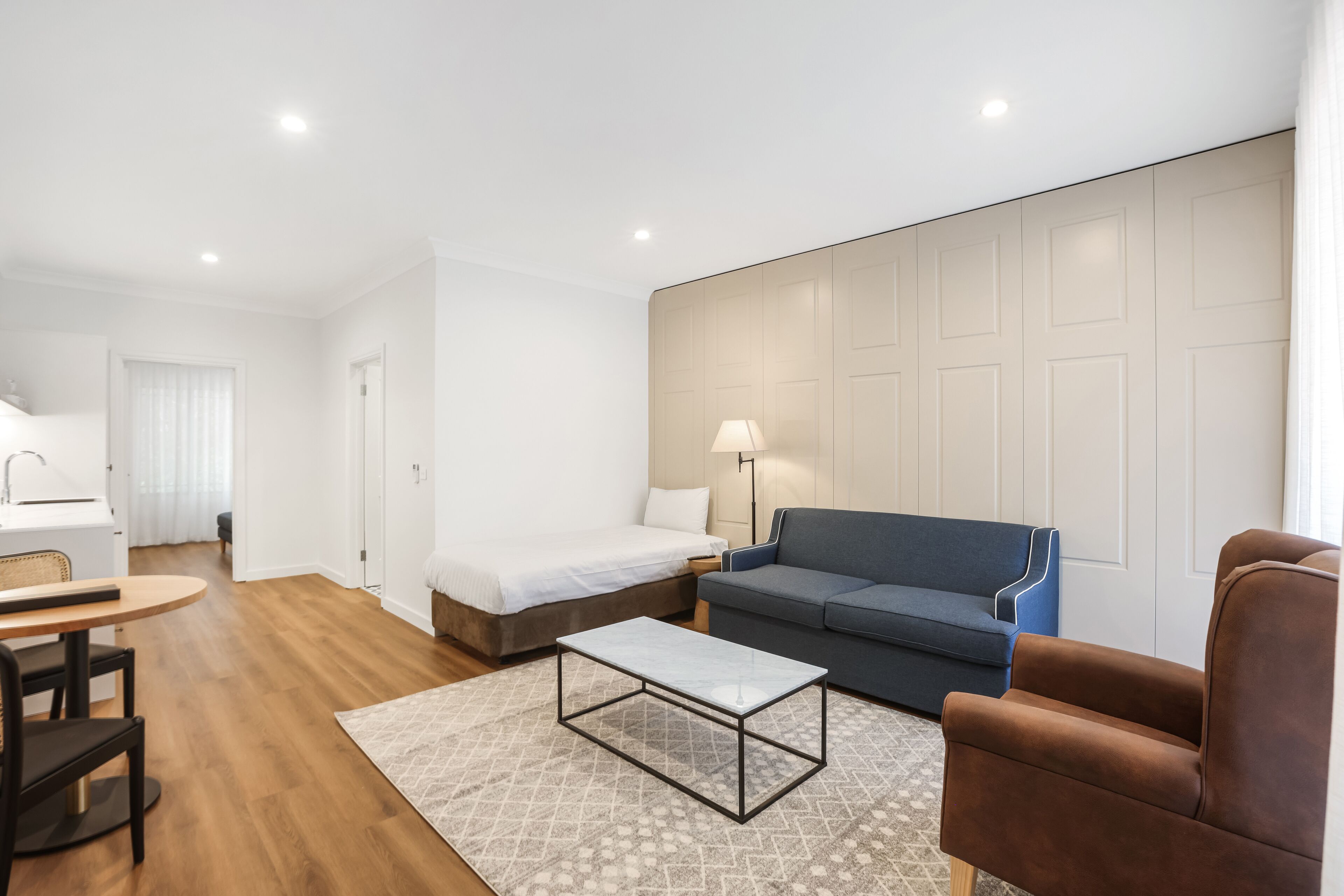 A modern hotel room with a bed, sofa, armchair, table, and lamp.