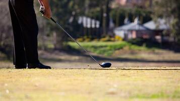 Une personne vêtue d’un costume sombre s’apprête à placer une balle de golf sur le green.