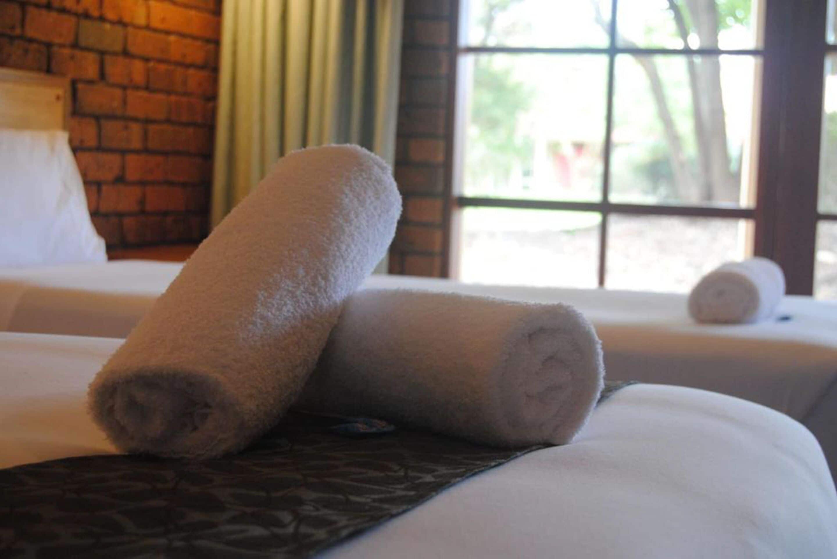 Habitación de hotel con pared de ladrillo, ventana con vistas y dos toallas enrolladas sobre la cama.