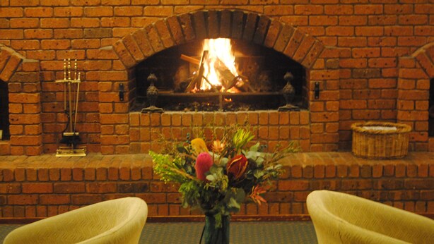 A brick fireplace with a fire, a vase with flowers, and two yellow chairs.