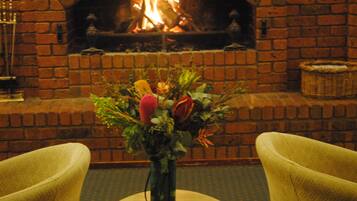 A room with a brick fireplace, a vase with flowers on a table, and two chairs.