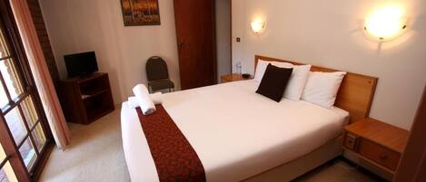 A hotel room with a large bed, a TV, a chair, a desk, and a painting on the wall.