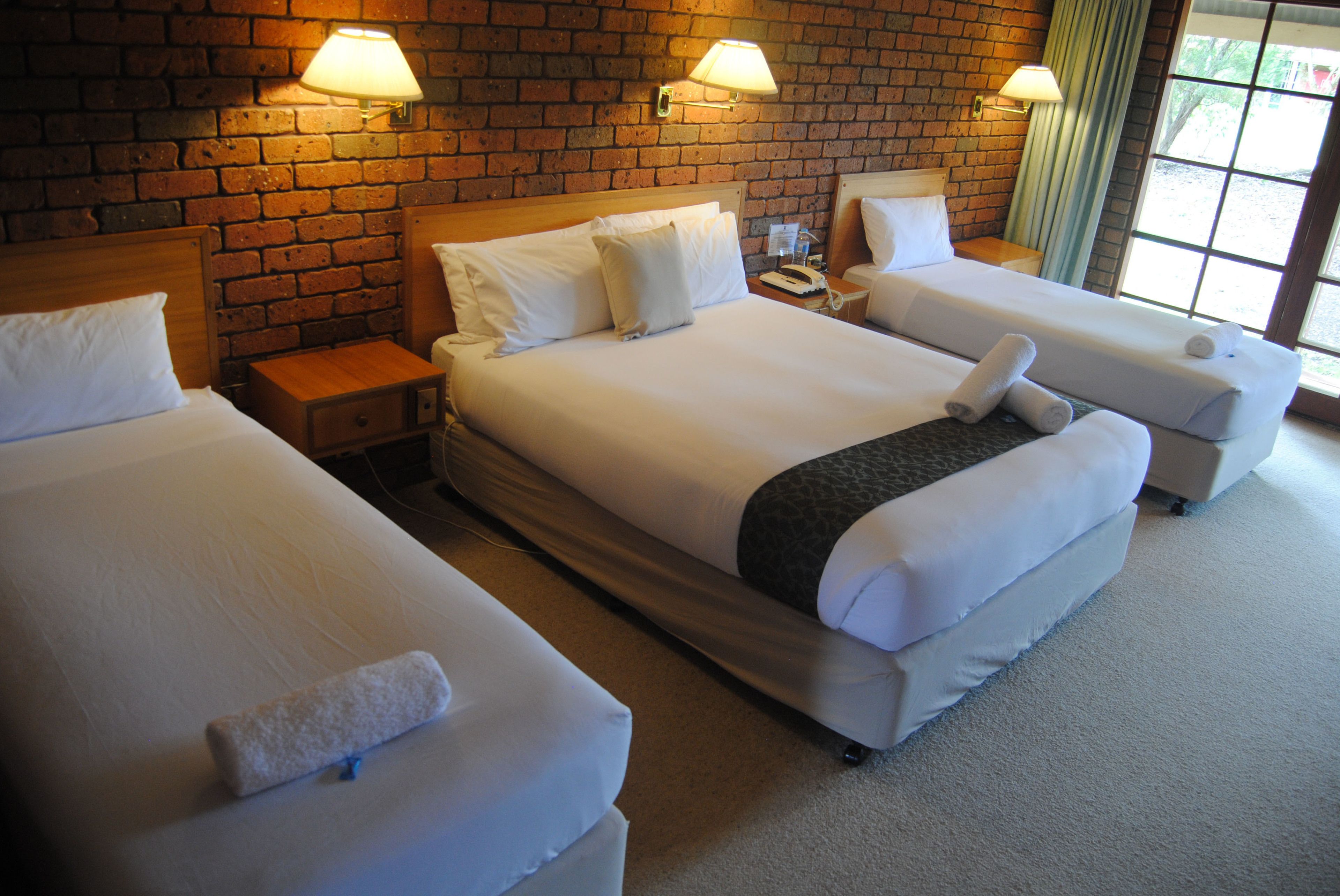 Habitación de hotel con dos camas, una pared de ladrillo y una ventana con cortinas.