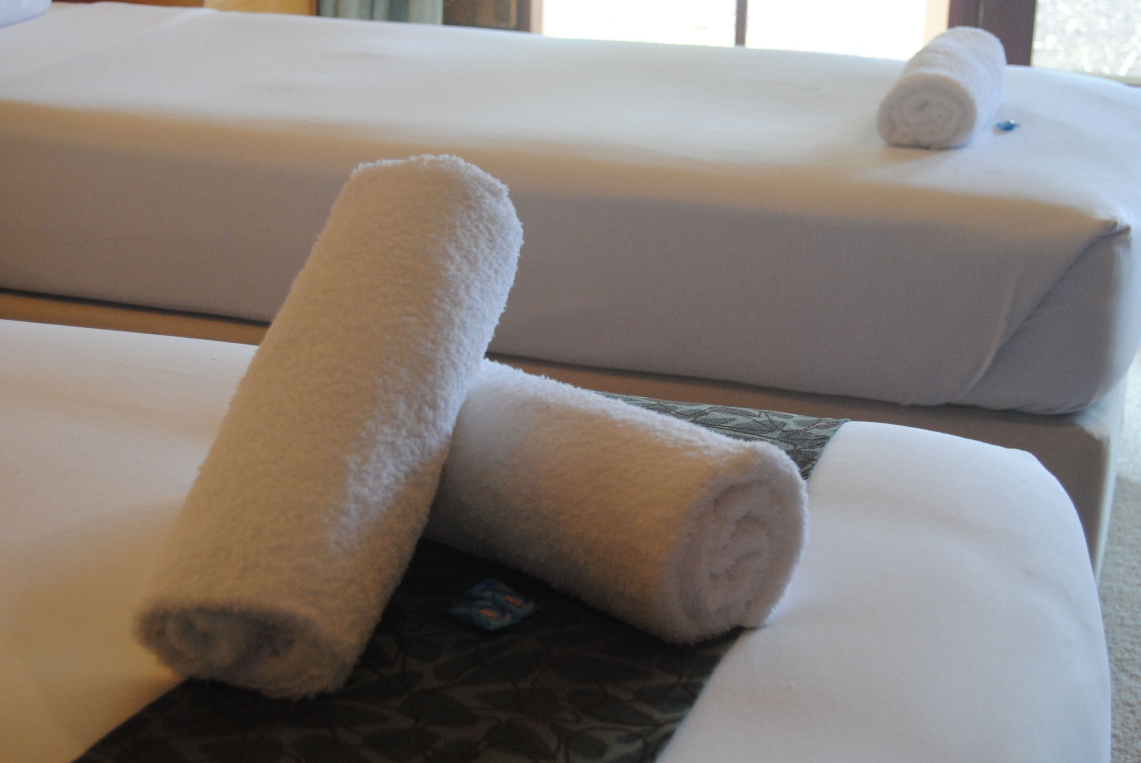 Two neatly rolled white towels on a bed with a patterned pillow.