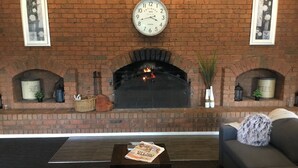 A living room with a brick fireplace, a clock, and a sofa.