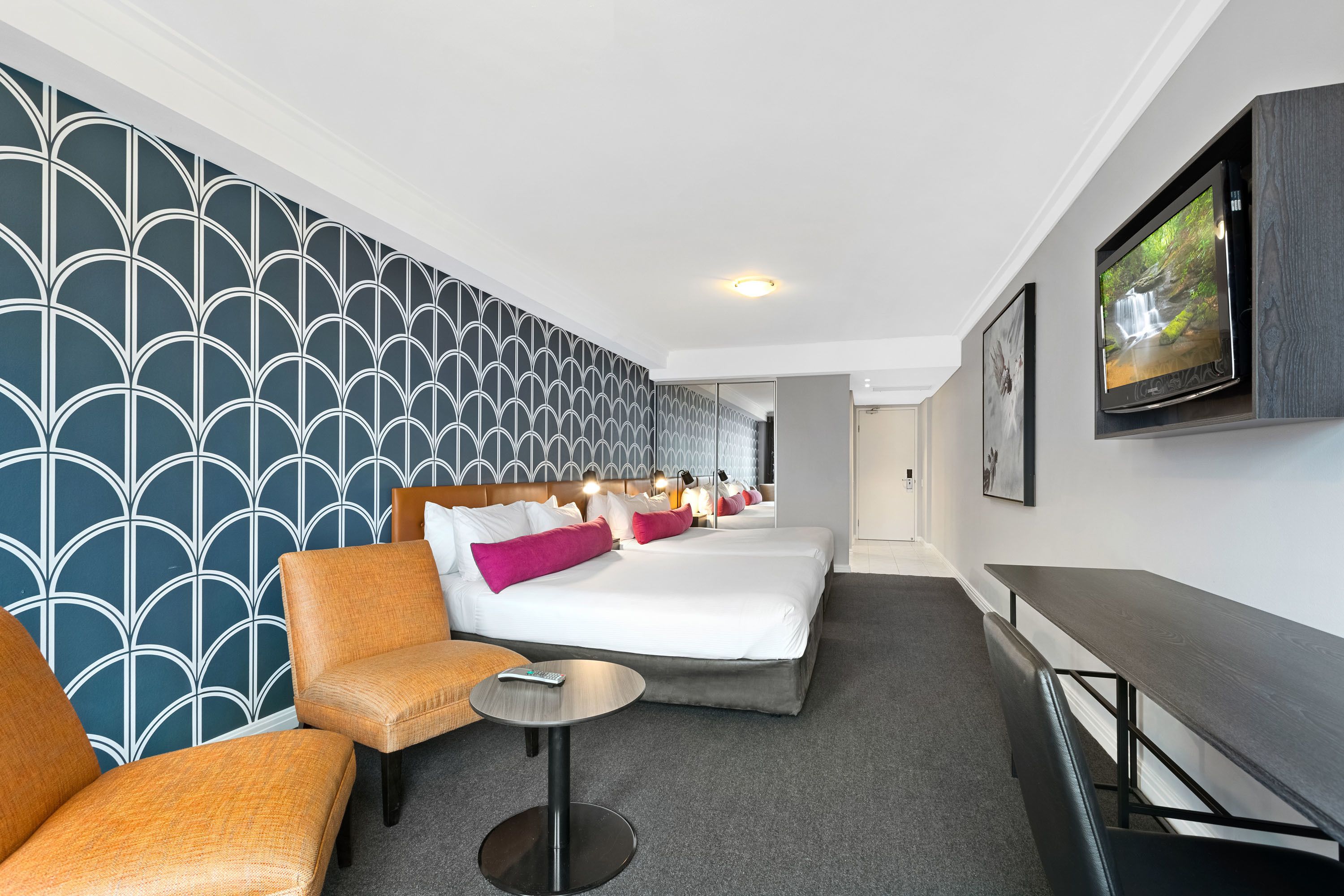 Una habitación de hotel con una cama grande, un sofá, una mesita y un televisor montado en la pared.