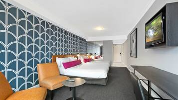 Una habitación de hotel con una cama grande, un sofá, una mesita y un televisor montado en la pared.