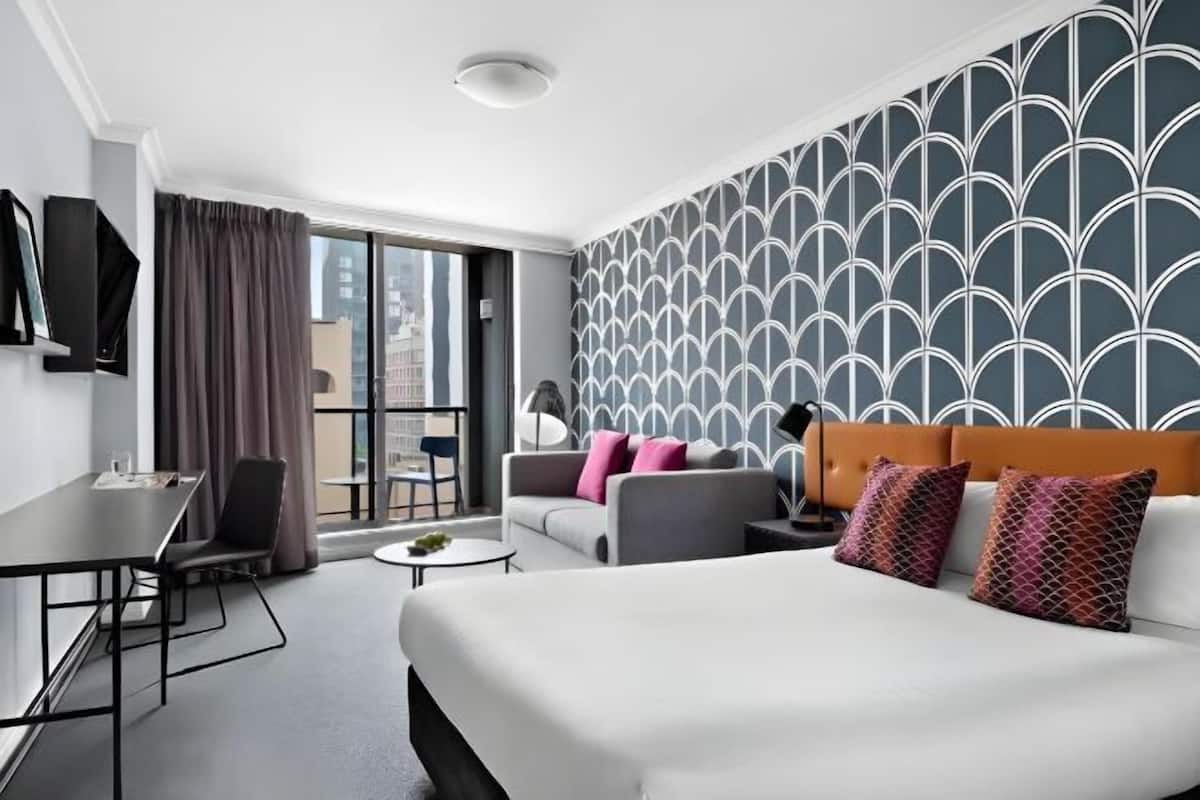 A hotel room with a bed, a sofa, a desk, and a chair.
